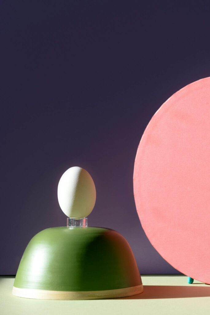 Abstract art piece featuring a bowl, egg, and colorful shapes against a purple background.